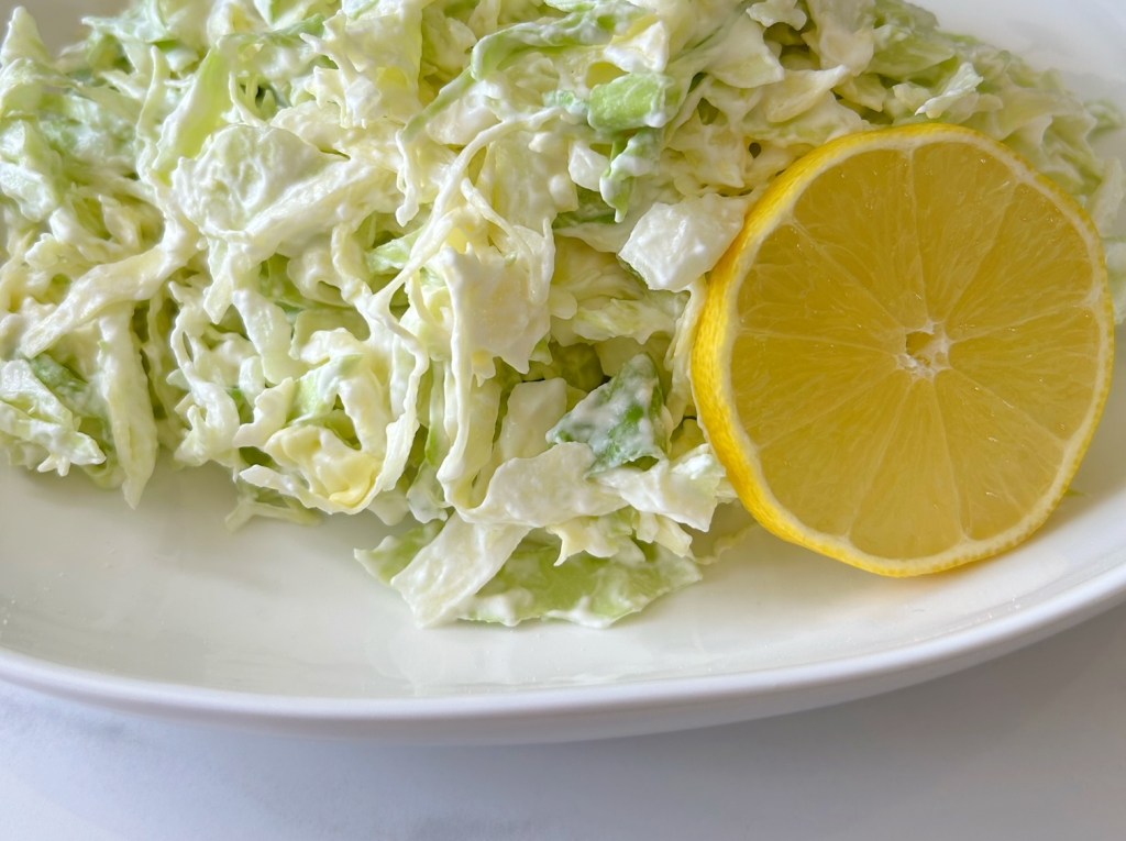 This is an image of cabbage salad.  The cabbage salad is in a bowl with a round slice of lemon.